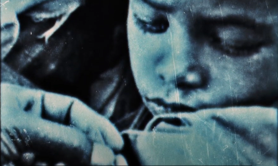 A black and white old photograph of a boy's face looking down at his arm.